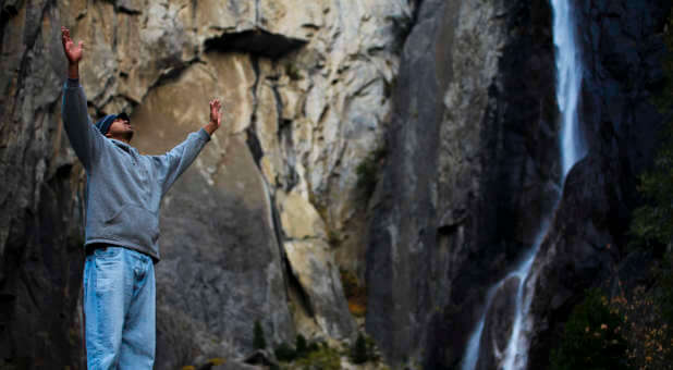 Hands raised in front of a waterfall