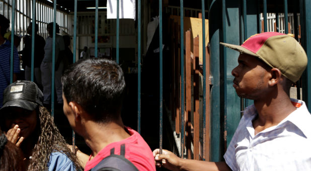 People queue to try to buy basic food items next to a paper that reads