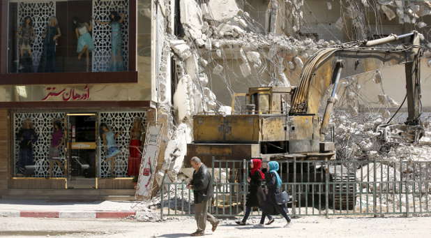 Palestinians walk past a demolished building in Gaza City April 14, 2016