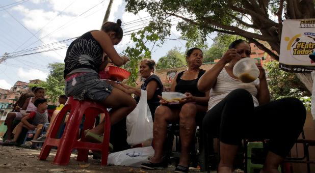 People eat free food which was prepared by residents and volunteers on a street in the low-income neighborhood of Caucaguita in Caracas