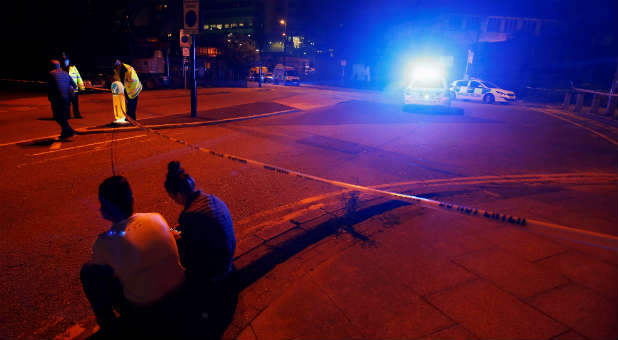 People sit by the side of the road next to a police cordon outside the Manchester Arena.