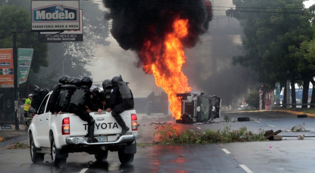Riot police officers travel past a burning police car during a protest against Nicaraguan President Daniel Ortega's government in Managua, Nicaragua.